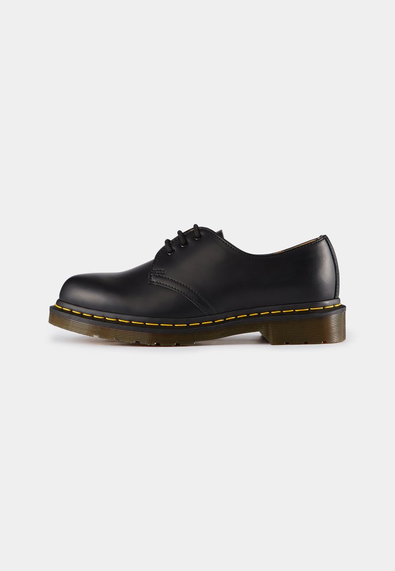 Shoe preto de couro com biqueira arredondada, design de atacador, costura amarela ao longo da sola e uma sola de borracha texturizada e robusta.