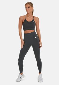 Dunkelgrauer Sport-BH und hochtaillierte Leggings aus Stretchmaterial. Die Leggings verfügen über ein Logo-Detail an der Hüfte und einen enganliegenden Schnitt.