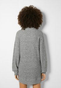 Stickad grå klänningströja med långa, puffiga ärmar, hög krage och ribbad textur; slutar ovanför knäna med en rak silhuett.