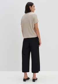 Beige geribde gebreide top met korte mouwen, textuurafwerking. Gecombineerd met zwarte wijde broek en sandalen met blokhak. Eenvoudige, moderne stijl.