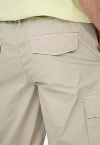 Bermudas de cargo beige hechas de tejido ligero, con dos bolsillos traseros y detalles de costura sutiles. Textura suave con un ajuste relajado.