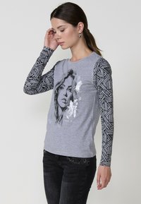 Camiseta de manga larga gris con una impresión de retrato en blanco y negro. Mangas negras con un diseño geométrico. Material de algodón suave.