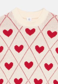 Megztinis iš mezginio, pagamintas iš kremine baze su raudonais širdies motyvais, išdėstytais rombo raštu, baigtas ribbalu ant apykaklės ir rankogalių.