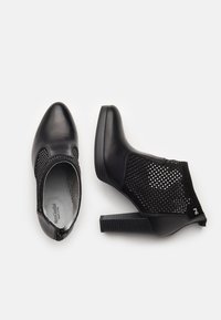 Para czarnych botków na wysokim obcasie za kostkę z perforowanymi siateczkowymi bokami oraz solidnymi obszarami na palce i pięty, wyeksponowanych na białym tle.