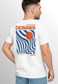 Weißes Baumwoll-T-Shirt mit einem bunten Grafikdesign auf dem Rücken – blaue Wellen, orangefarbene Sonne und Text, der "OKINAWA" und "Kyūshū" sagt.