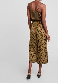 Top in satin oliva con spalline sottili abbinato a pantaloni larghi marroni con un motivo a stampa leopardata nera e una vita arricciata.