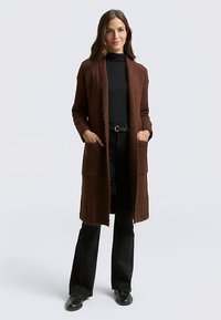 Bruine gebreide cardigan met een open voorkant, lange mouwen en twee zakken aan de voorkant; geribbelde textuur bij de manchetten en onderzoom.