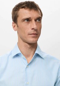 Svijetloplava košulja na pruge izrađena od tkanine glatke teksture. Ima standardni ovratnik i kopčanje na gumbe, sa uskim okomitim prugama.