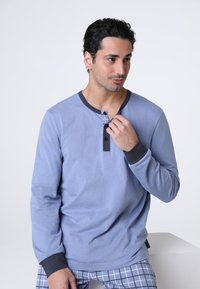 Camicia blu a maniche lunghe con colletto scuro a contrasto, patta frontale con bottoni e polsini aderenti. Tessuto morbido e vestibilità rilassata.