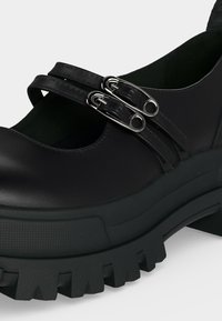 Chaussure Mary Jane noire à plateforme avec double brides attachées par des boucles argentées en forme d'épingle à nourrice et semelle épaisse texturée.