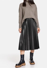 Maglione a collo alto in beige chiaro, abbinato a una gonna in pelle nera plissettata a vita alta e stivaletti neri con suola spessa.