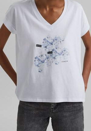 Witte V-hals T-shirt met blauw-witte bloemenprint en tekst "keep life simple," gedragen met donkergrijze spijkerbroek.