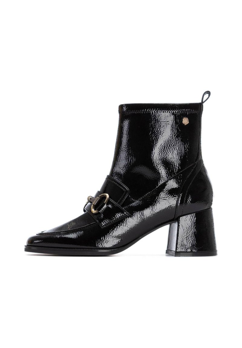Botín de cuero sintético negro con puntera cuadrada, tacón grueso, hebilla decorativa y acabado texturizado. Presenta una lengüeta en la parte trasera.