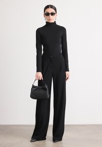 Maglione a collo alto nero, pantaloni a gamba larga con chiusura a bottone e una borsa nera testurizzata. Occhiali da sole eleganti e calzature a contrasto completano l'outfit.