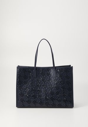 Bolso tote de cuero cortado con láser en azul marino, con dos asas, forma rectangular, patrón geométrico intrincado y parte superior abierta. Textura suave.
