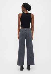 Viddejeans i mørkegrå med et subtilt bølgemønster, paret med en svart ermeløs topp. Glatt tekstur og høy midje-design.