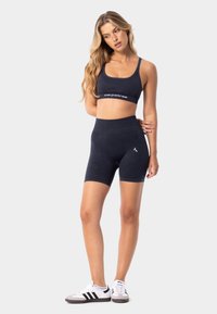 Soutien-gorge de sport noir et short de vélo taille haute assorti en tissu doux, avec un logo sur la bande du soutien-gorge et sur le short, et des accents contrastants.
