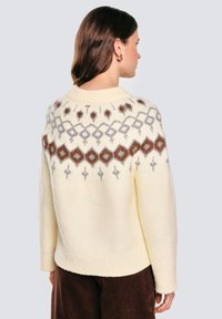 Sweter w kolorze kremowym z geometrycznym wzorem w brązowym, szarym i różowym kolorze wokół karczku. Miły w dotyku, z prążkowanymi mankietami i detalem u dołu.