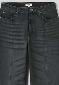 Jeans en denim noir à taille haute, avec cinq poches et des accessoires en argent. Coutures visibles et coupe droite avec une texture subtile.
