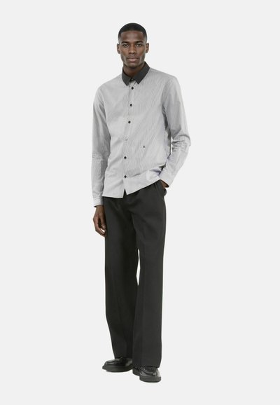 Camisa a rayas en blanco y negro con cuello negro, combinada con pantalones negros holgados y zapatos negros. Corte ajustado, mangas largas.