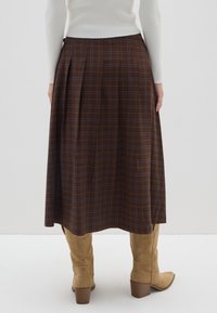 Bruine geruite midi-rok met plooien, gemaakt van een gestructureerde stof. Gecombineerd met tan kleurige suède laarzen tot de knie met een chunky hak.