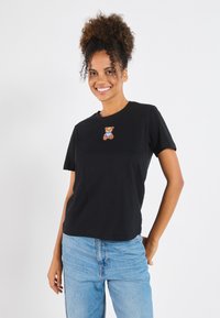 Black cotton t-shirt featuring a small embroidered teddy bear detail on the chest. Slim fit with short sleeves and a crew neckline.