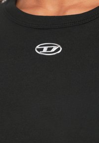 Melnas krāsas T-krekls no gludas auduma ar apaļu kakla izgriezumu un mazu sudraba logo uz krūtīm. Vienkāršs dizains, pieguļošs siluets.