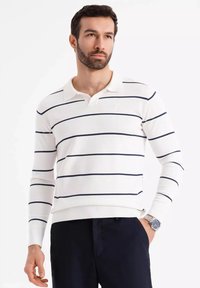 Polo a maniche lunghe bianco a righe, con strisce orizzontali blu navy, colletto, polsini a costine e design aderente. Indossato con pantaloni blu navy.