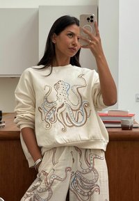 Krémová mikina s modro-hnedým dizajnom chobotnice, doplnená o zladené nohavice s podobnými vzormi. Mäkký bavlnený materiál, voľný strih.