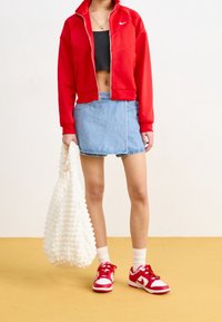 Röd zip-up jacka, svart crop top, denim mini kjol, vit texturerad handväska och röda sneakers med vita detaljer. Helt avslappnad look.