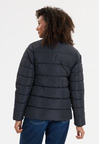 Svart puffjacka med horisontell sömnad, långa ärmar och avslappnad passform. Slät textur, lätt design, lämplig för svalt väder.