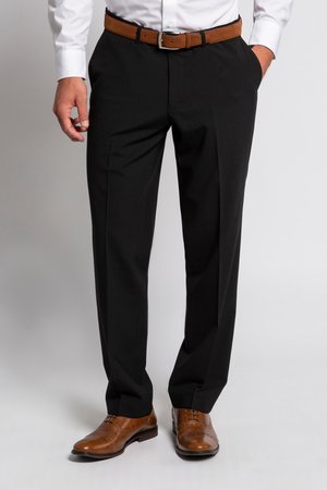 Mężczyzna w czarnych eleganckich spodniach, brązowym skórzanym pasku i pasujących brązowych eleganckich butach sznurowanych, stoi z jedną ręką w kieszeni.