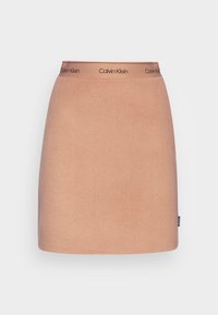 Sukně Calvin Klein z měkké broskvové tkaniny, v rovném střihu, s kontrastním páskem s logem. Jednoduchá, bez dalších vzorů nebo akcentů.