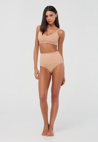 Set di reggiseno beige e slip a vita alta realizzato in tessuto morbido. Il reggiseno presenta spalline sottili e un design a V. Texture morbida in tutto il capo.