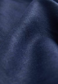 Gros plan sur un tissu doux bleu foncé avec une texture tissée fine et de légers plis créant des variations de lumière et d'ombre.