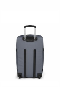 Valise en tissu gris avec une poignée rétractable, deux bandes noires en accent et quatre roues pour la mobilité. Fermeture éclair en haut.