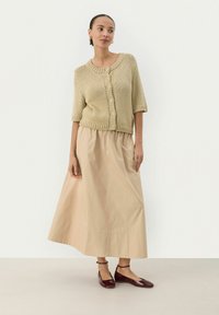 Cardigan en tricot beige à manches courtes et boutons, associé à une jupe maxi fluide crème et des ballerines bordeaux. Textures de tissu lisses.