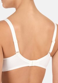 Bra bianco senza cuciture con spalline regolabili, chiusura a gancio e occhiello sul retro e una texture liscia e piatta. Design minimalista e modellante.