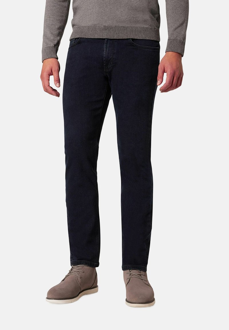 Dunkelblaue Slim-Fit-Jeans aus Denim, kombiniert mit einem hellgrauen Pullover und beigen Wildlederschuhen. Das Outfit hat ein einfaches, lässiges Design.