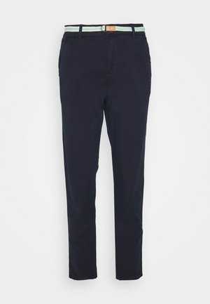 Pantalones casuales de hombre azul marino con un cinturón de tela trenzado blanco y verde claro sobre un fondo liso.