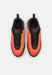 Nike sportcipők, amelyek narancs és fekete színátmenetes felsőrésszel rendelkeznek, texturált anyagból készültek, fekete fűzőkkel és piros hangsúlyos logóval a nyelvén.