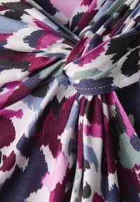 Tissu multicolore présentant un motif floral dans des tons de violet, noir et rose, avec un détail en nœud tordu au centre.