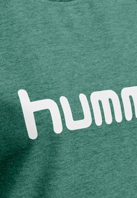 Felpa verde melange con collo rotondo e prominente logo bianco "humm" stampato sul davanti. Tessuto morbido e design informale.
