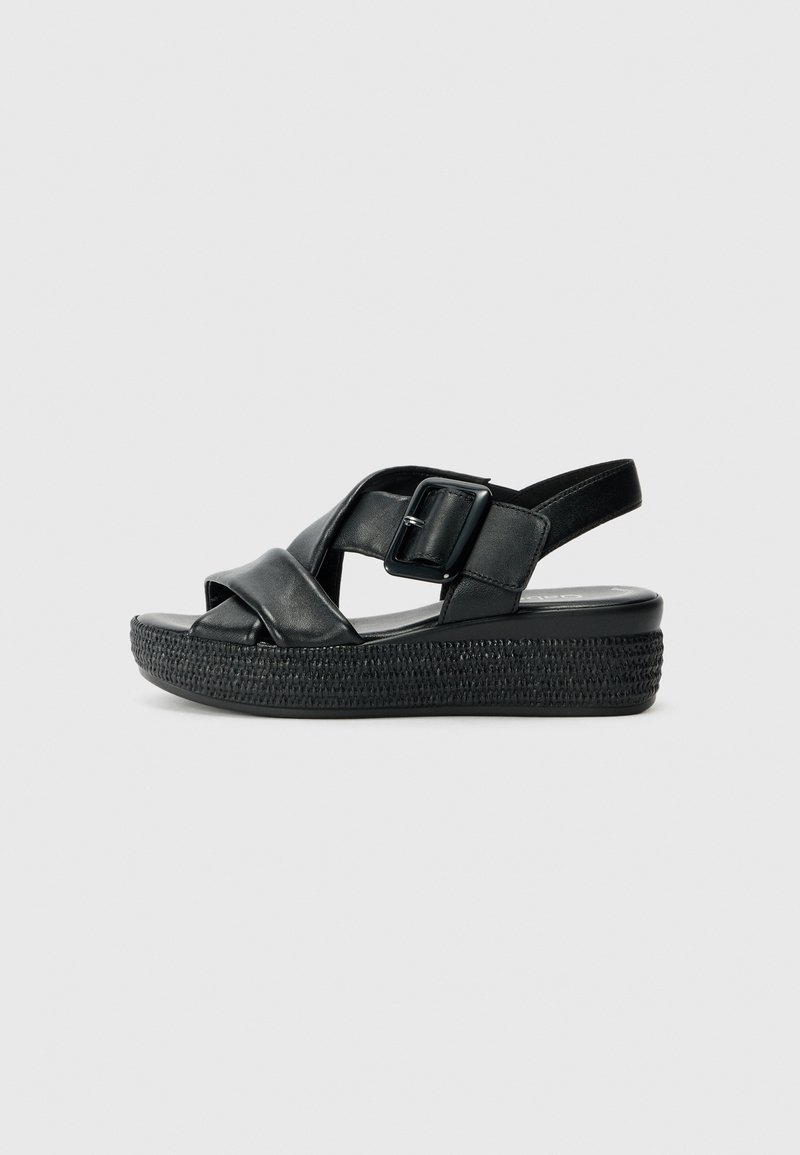 Sandales en cuir noir avec une plateforme tressée, présentant des brides croisées et une fermeture à boucle sur le côté. Texture lisse, design ouvert à l'avant.