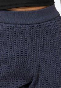 Pantalon texturé bleu marine avec un motif ondulé, doté d'une taille côtelée. Le matériau semble léger et respirant.