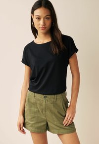 Camiseta negra de manga corta con cuello redondo, combinada con pantalones cortos de talle alto en color verde oliva que cuentan con grandes bolsillos laterales y cierre de botón.