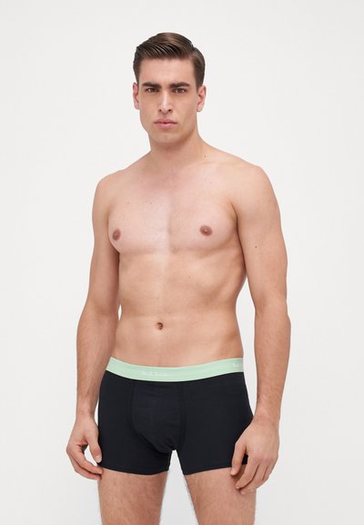 Boxer-culottes noires avec une taille en vert clair arborant le nom de la marque. Tissu lisse, design ajusté et sans motifs visibles.