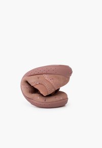 Zapato flexible rosa para toddlers con una parte superior suave y texturizada y suela de goma. Cuenta con una correa de velcro y pequeñas motas decorativas.