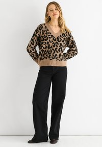 Leopard print sweater in beige and black, V-neck design, loose fit, ribbed hem and cuffs, paired with black wide-leg pants.