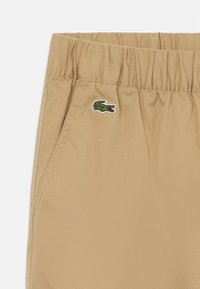 Khaki shorts med elastisk midje, med sidelommer og en liten grønn krokodillelogo brodert på venstre front.